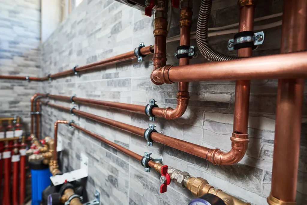 Copper water supply lines with soldered elbows clamped to a tiled wall