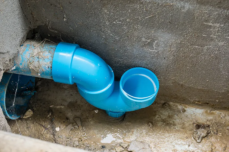 Blue U-shaped PVC trap fitting on a drain line against a concrete wall