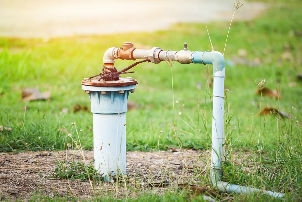 Private well head with a rusted fitting and a blue water line running across a grassy yard