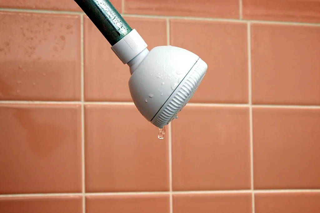 White shower head against peach tile with only a few drops of water coming out
