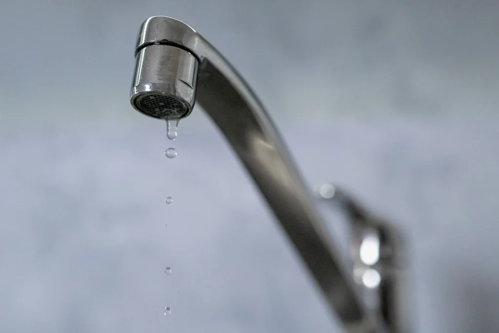 Chrome kitchen faucet with a thin trickle of drops falling from the aerator