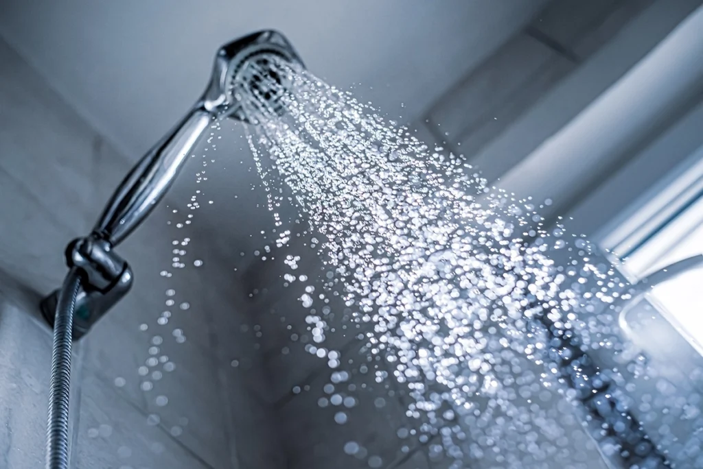 Handheld shower head spraying water in a gray tiled shower