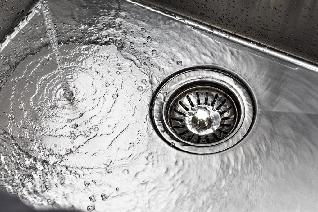 Water swirling across a stainless steel kitchen sink toward the strainer drain