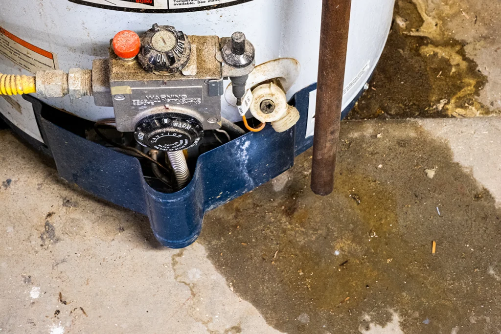 Base of a gas water heater and its control valve, with a water stain spreading across the concrete floor