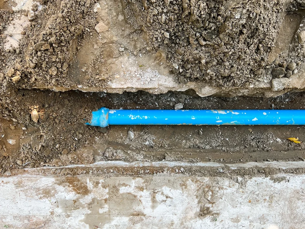 Blue water supply pipe exposed in an excavated trench of soil and gravel