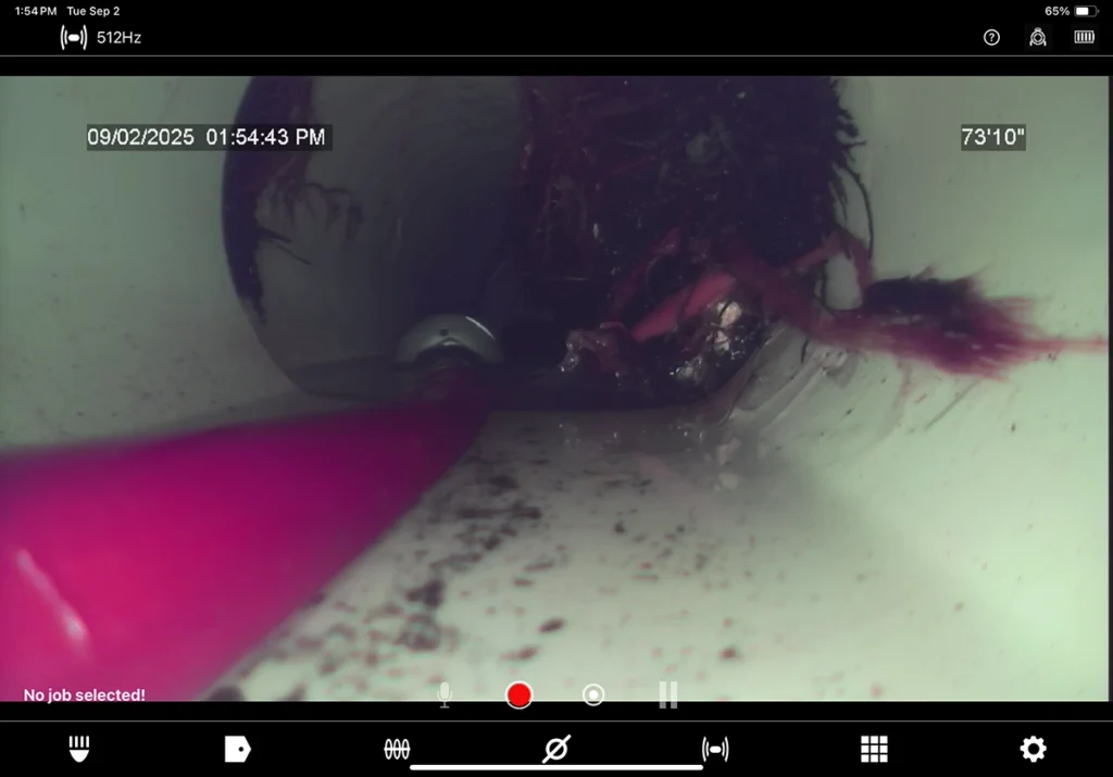 Sewer camera monitor showing a dark blockage inside a drain pipe