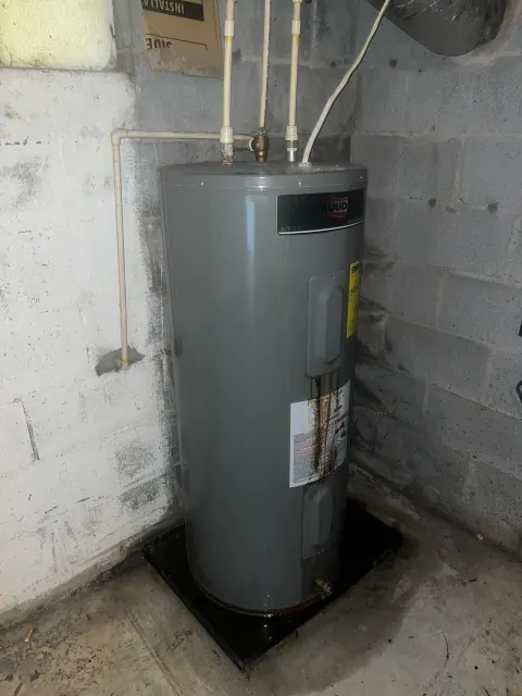 Before: Rust-streaked gray electric water heater on a black pan against a block basement wall