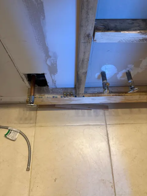 After: New chrome shutoff valves on the sink and toilet supply lines along the opened wall