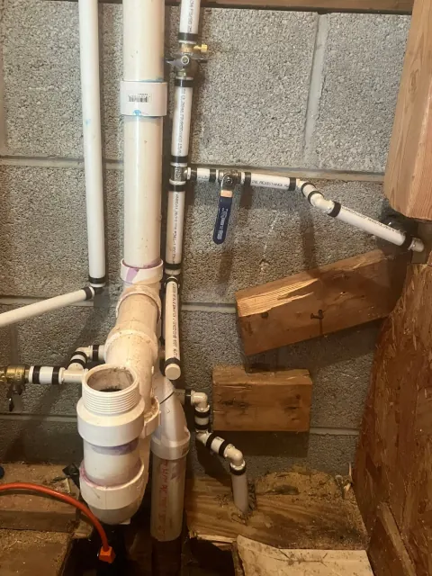 After: New white supply lines with black fittings and a blue-handled ball valve beside the same drain pipe