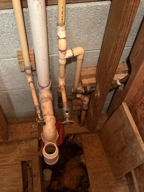 Before: Older tan supply pipes and corroded valves beside a white drain pipe against a block wall