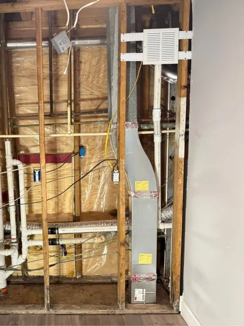 After: The same open wall with the corrected vent pipe rising to a white grille box near the ceiling
