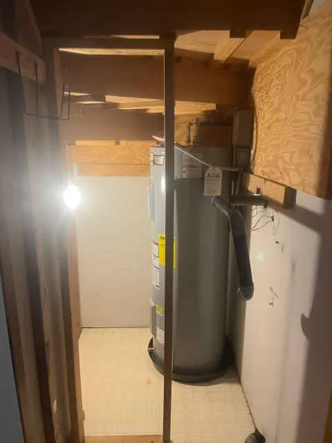 After: New gray water heater on a drain pan in the same closet, lit by a work light