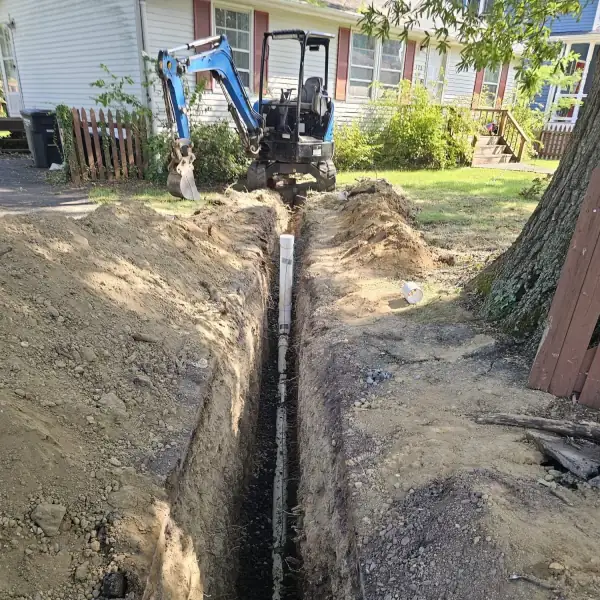 Mini-excavator at the end of a long open trench with new sewer pipe laid.