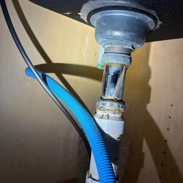 Before: Corroded metal drain tailpiece leaking under a vanity sink.