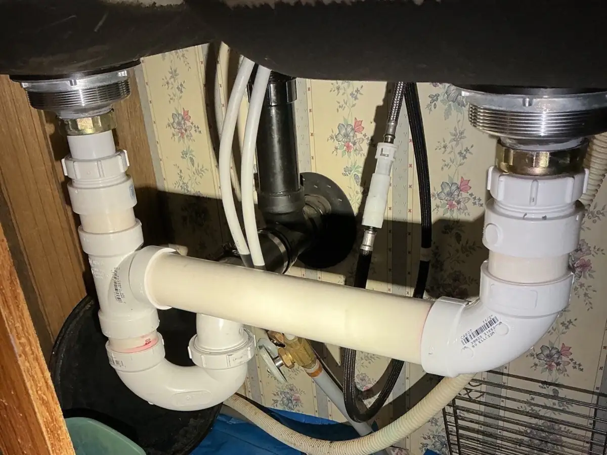 New white PVC drain lines installed under the kitchen double sink.