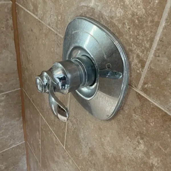 Before: Old shower valve trim on a tiled wall with a drip.