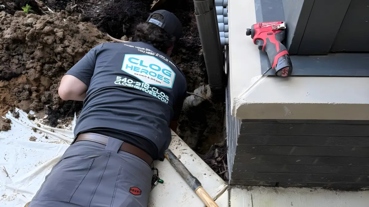 Technician lying on a patio digging at a foundation, Clog Heroes logo on his back.