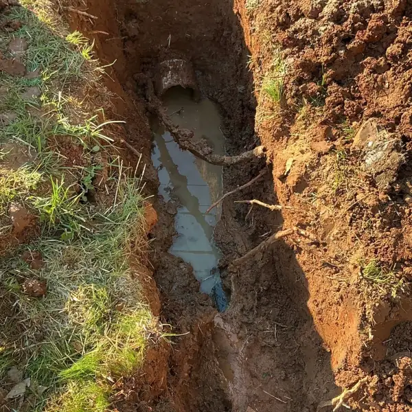 Broken sewer line uncovered in a wet trench.